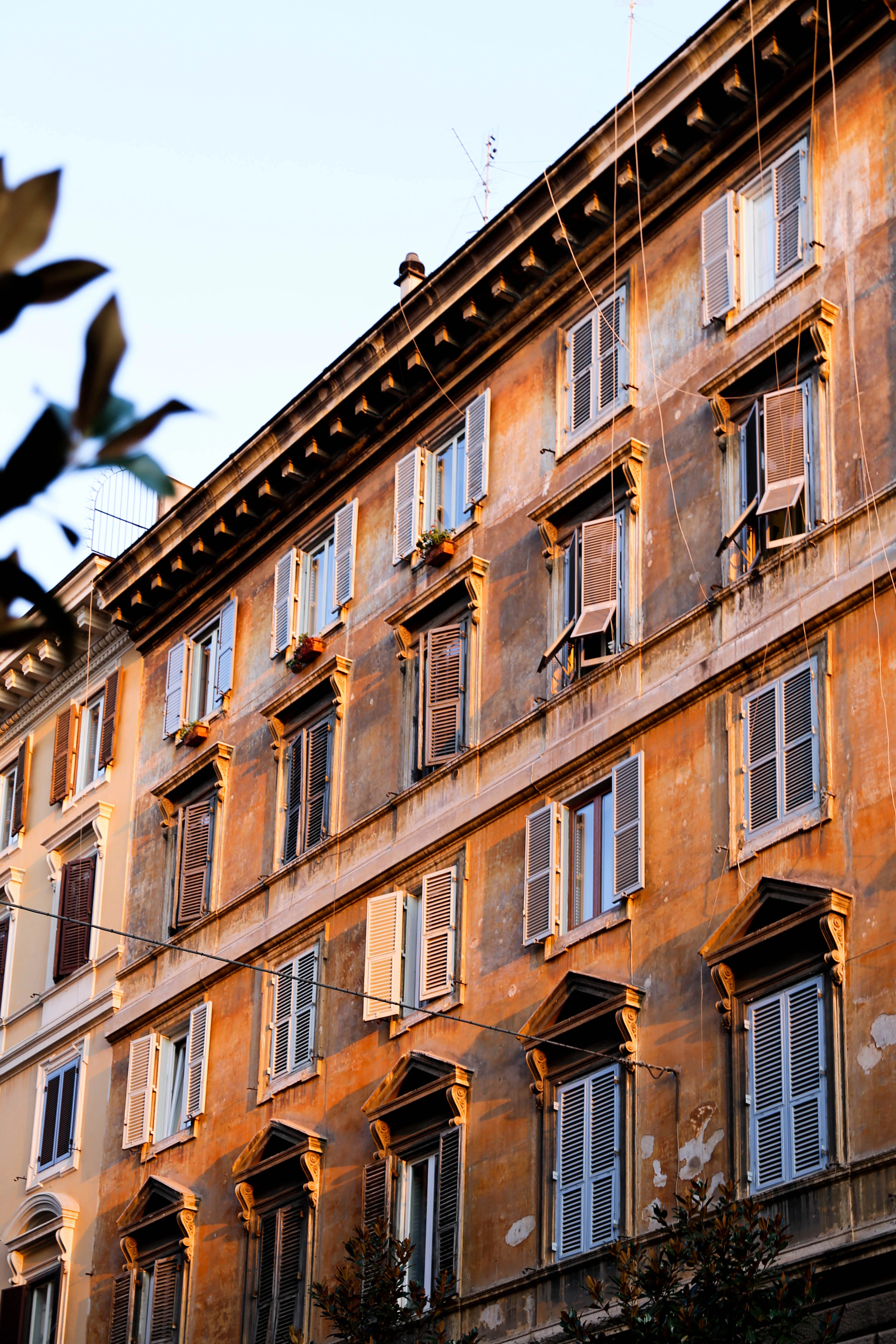 A terracotta coloured building with rows of windows and shutters.