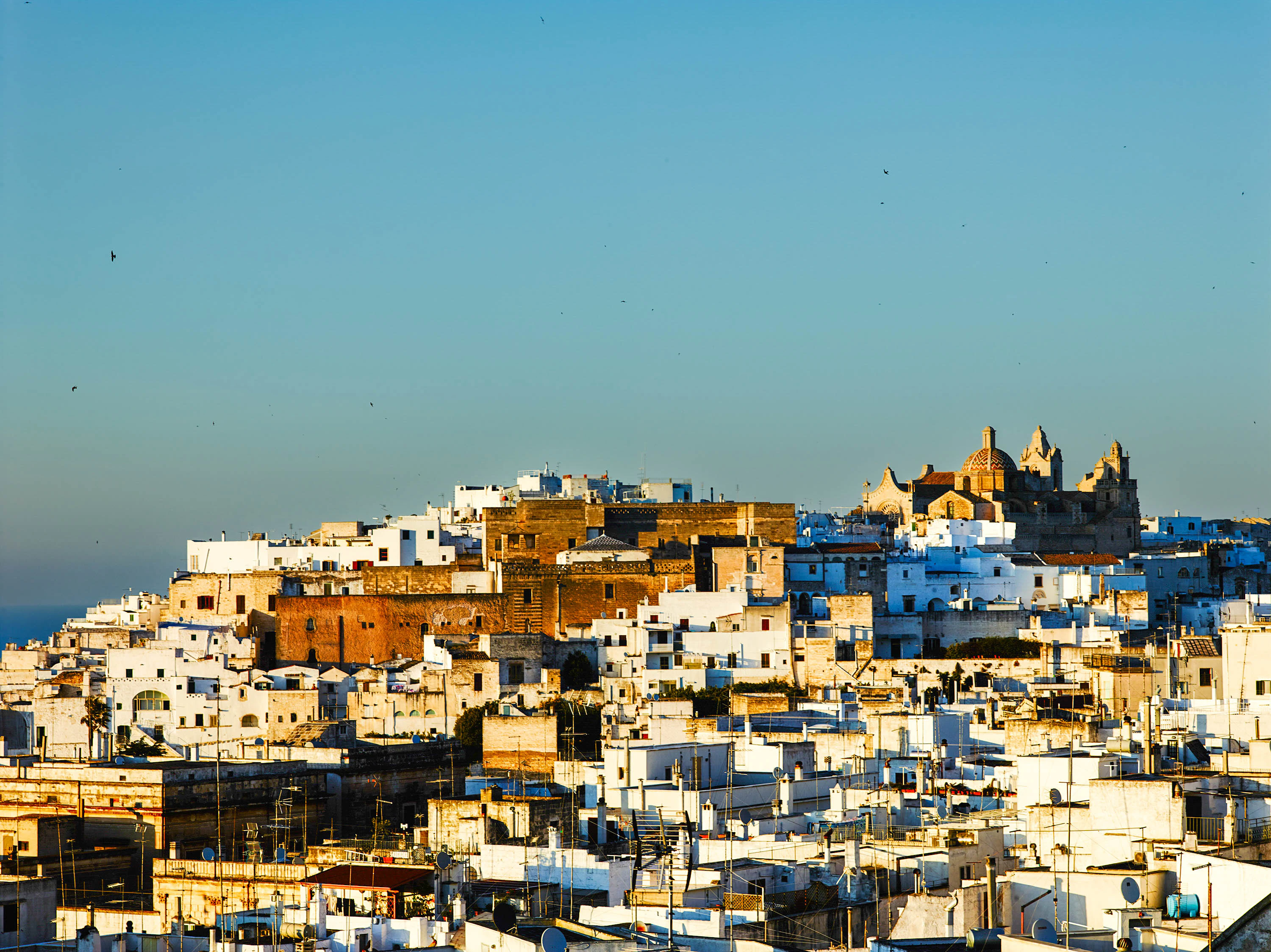 A town sits perched on the top of a hill against a blue sky.