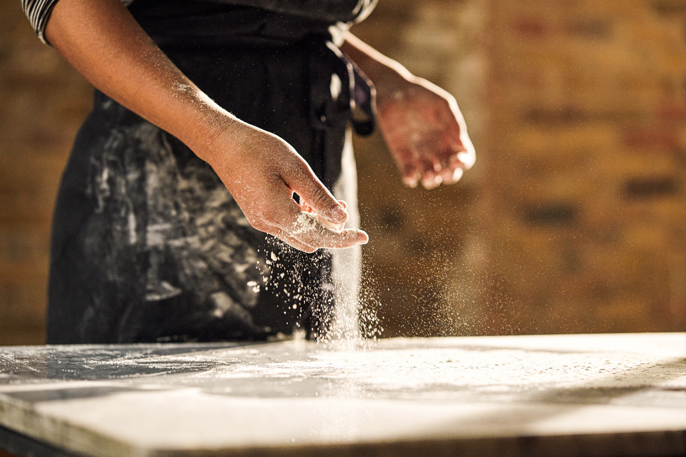A aproned person scatters flour over a marble surface.