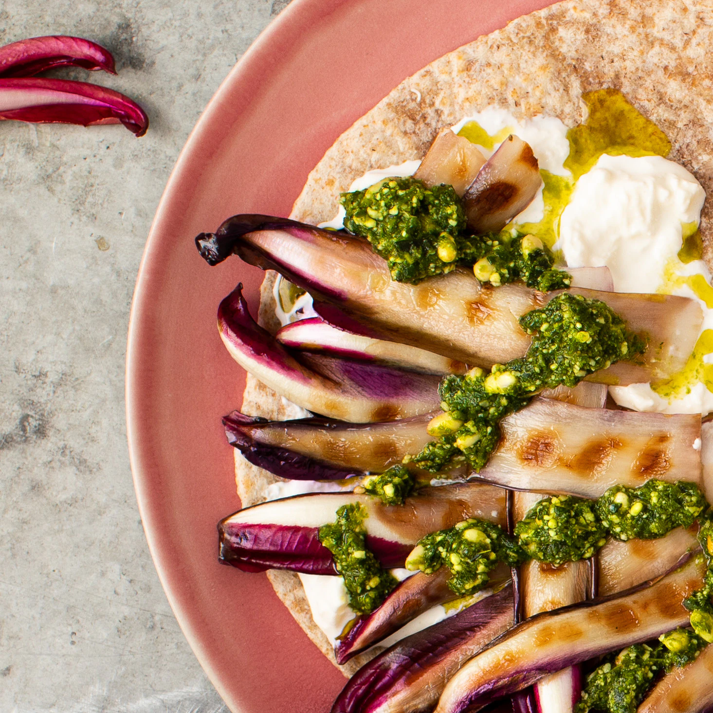 A pink plate with a piadina filled with radicchio, burrata and pesto on it.