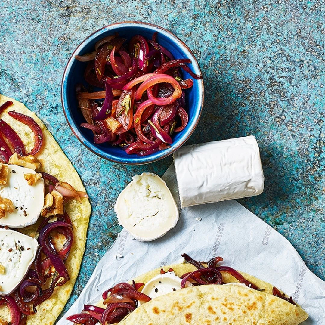 A bowl of caramelised red onions is next to a log of goats cheese.