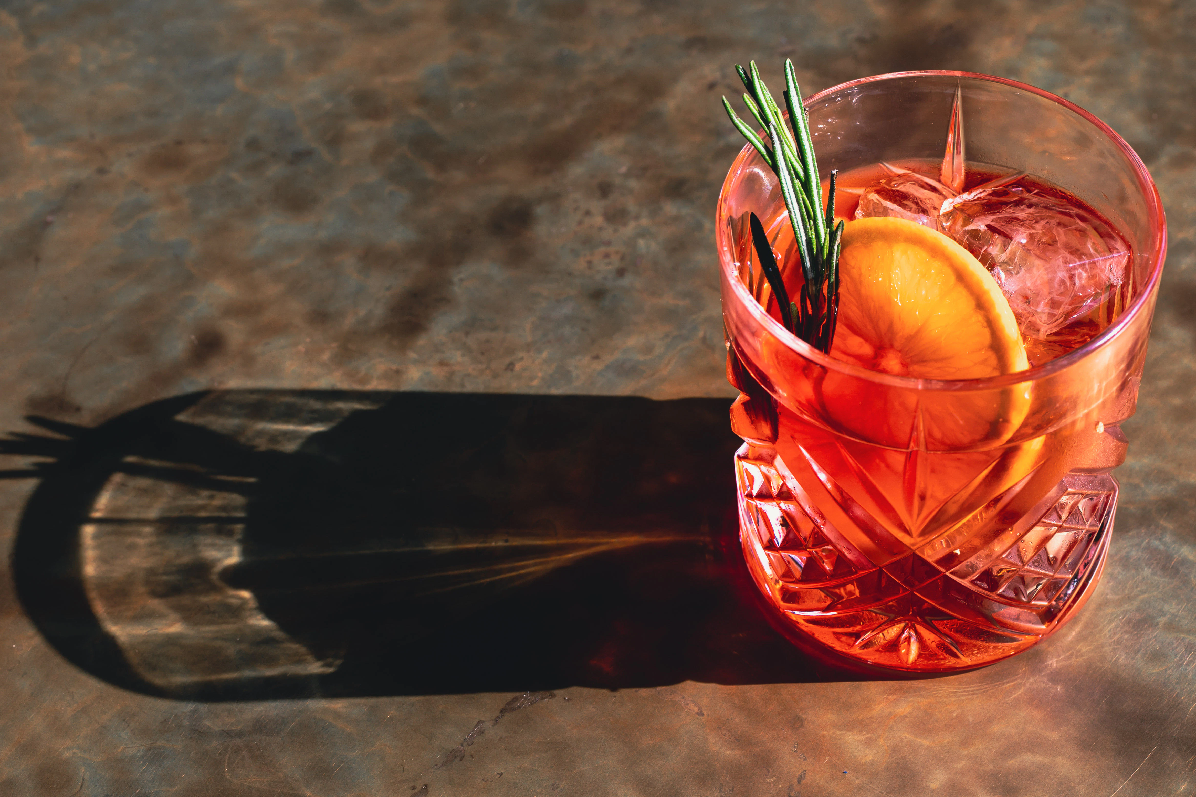 A red drink garnished with rosemary and a lice of orange.