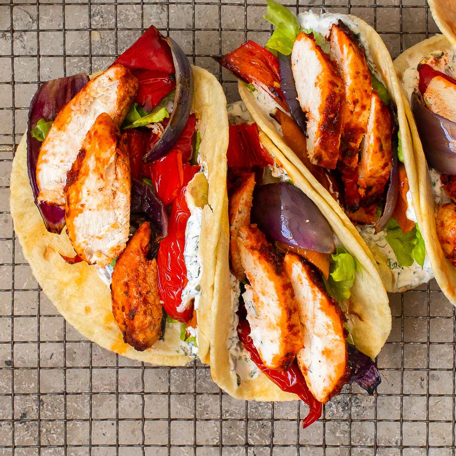 Three mini piadina on a rack, filled with lettuce, grilled vegetables, chicken and yoghurt.