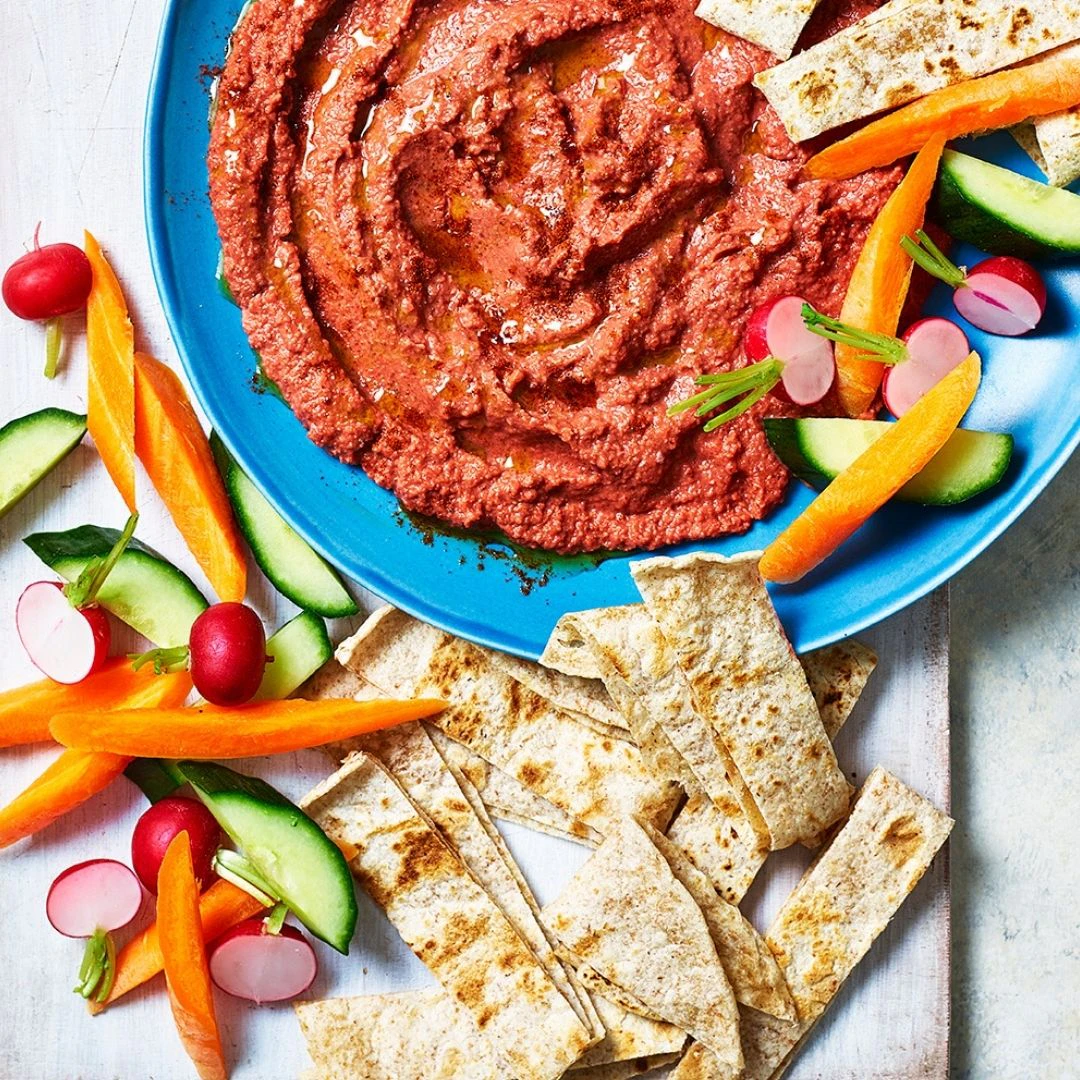 A bowl of beetroot hummus with slices of Organic Wholeblend Piadina and vegetable crudités round the edge.