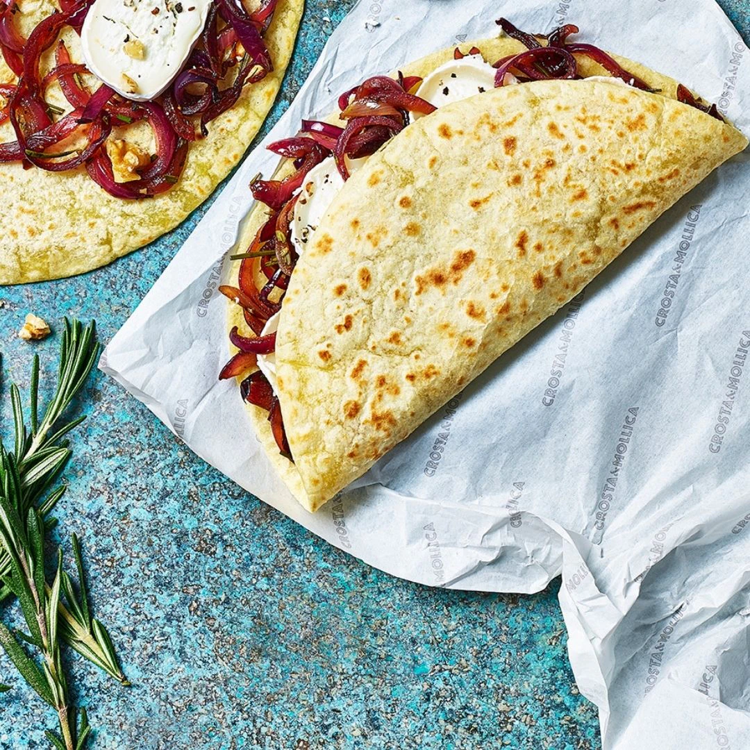 A folded Piadina Emiliana filled with goats cheese, caramelised red onions and walnuts is in shot.
