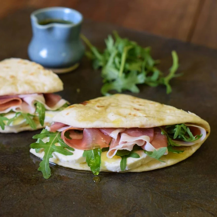 A Piadina stuffed with rocket, mozzarella and prosciutto is folded in half, and cut open.
