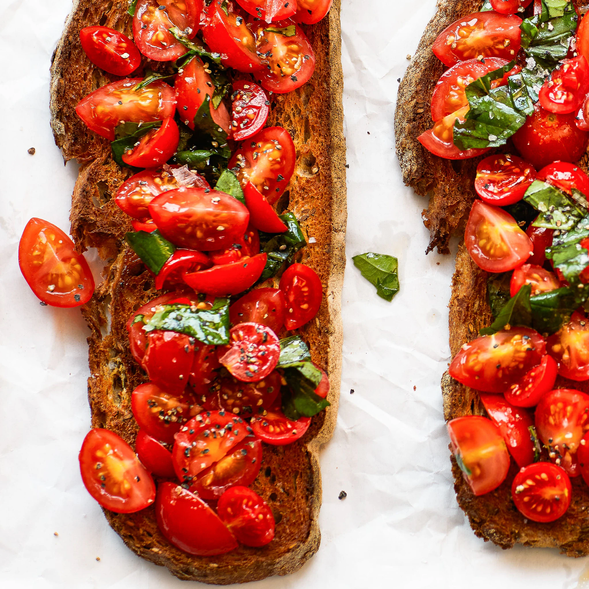 A slice of pane Pugliese bread topped with sliced tomatoes and fresh basil.