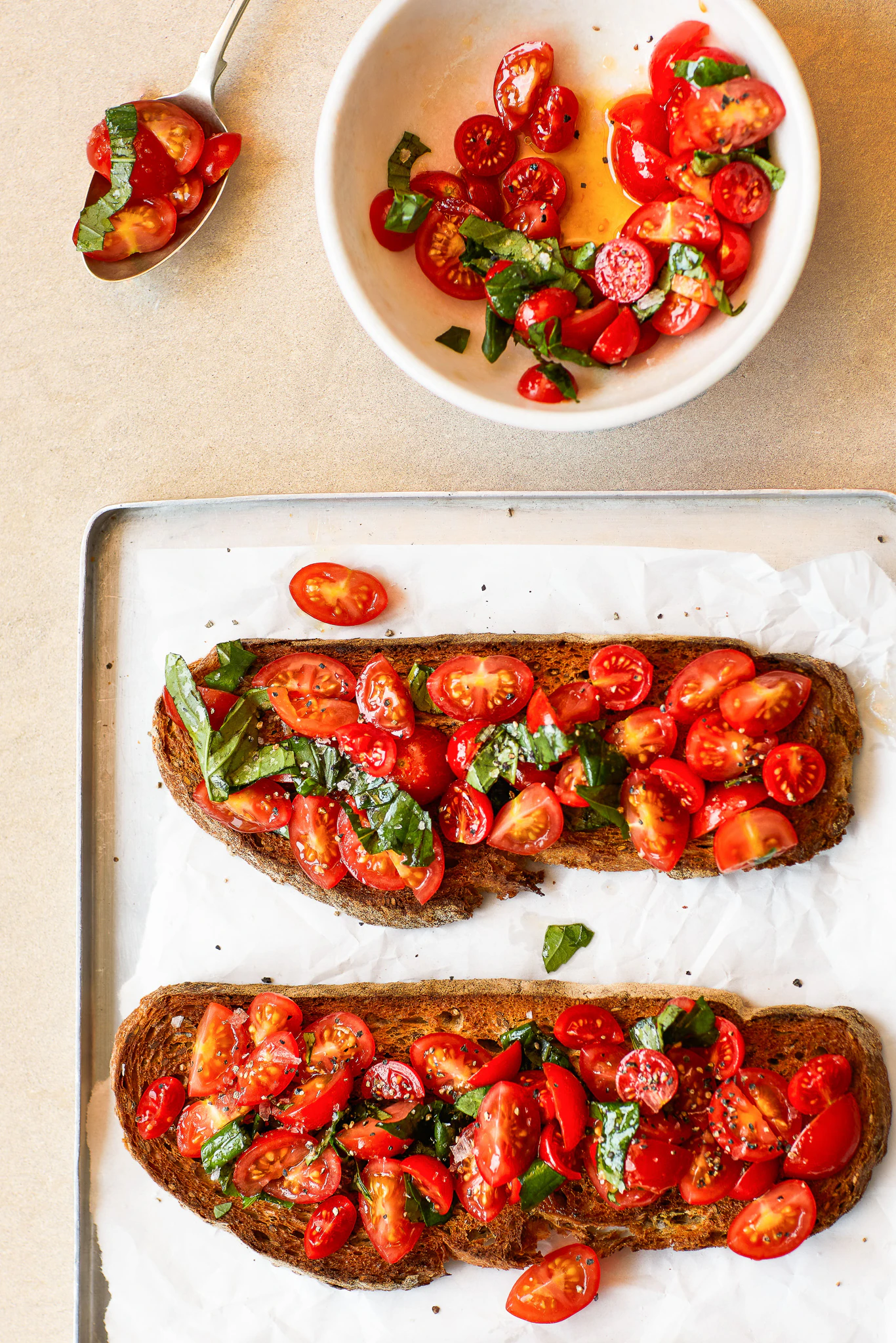 Two slices of pane Pugliese topped with tomatoes are on a tray next to a bowl of sliced tomatoes.