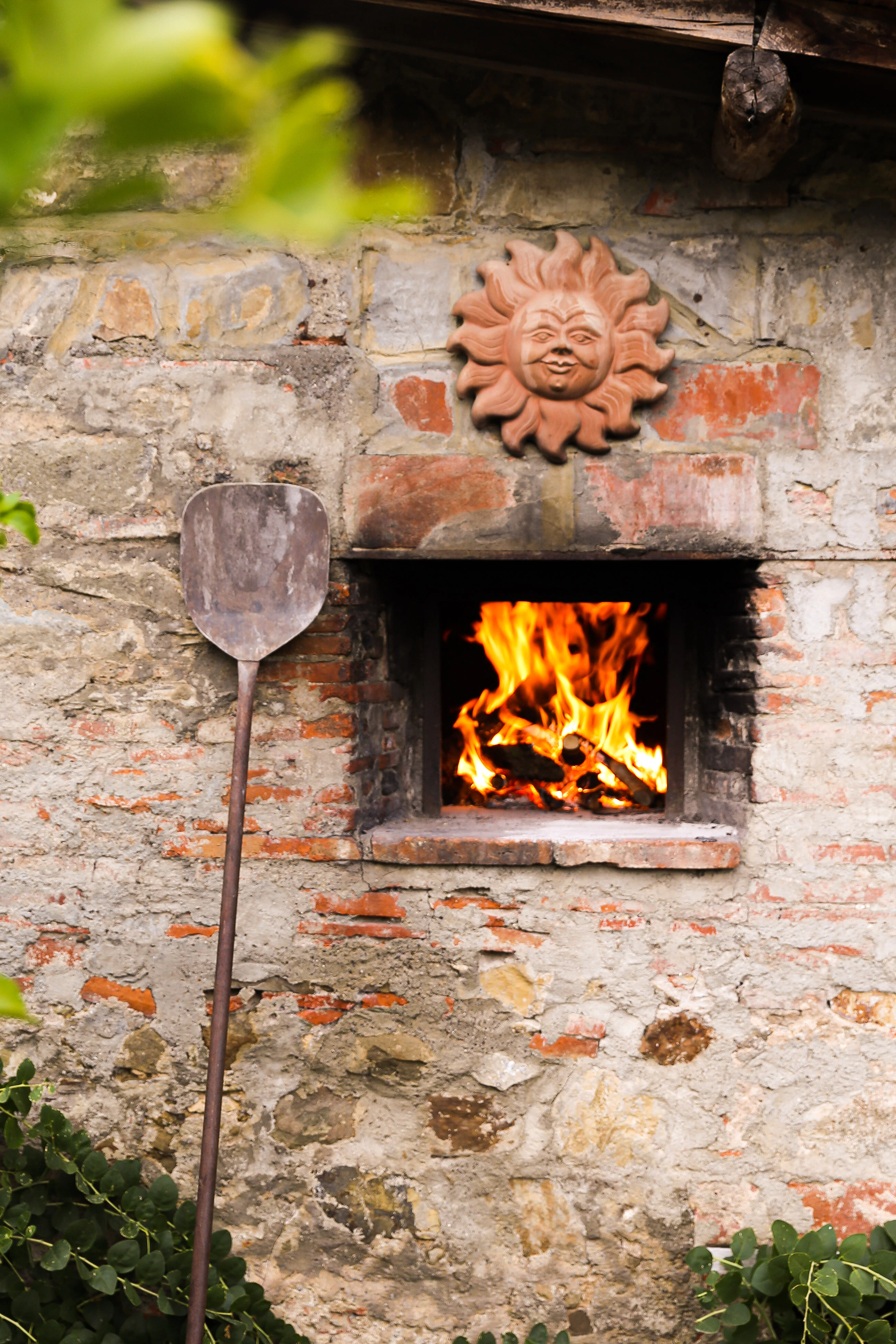 A small pizza oven in a brick wall, a pizza peel is against the wall.