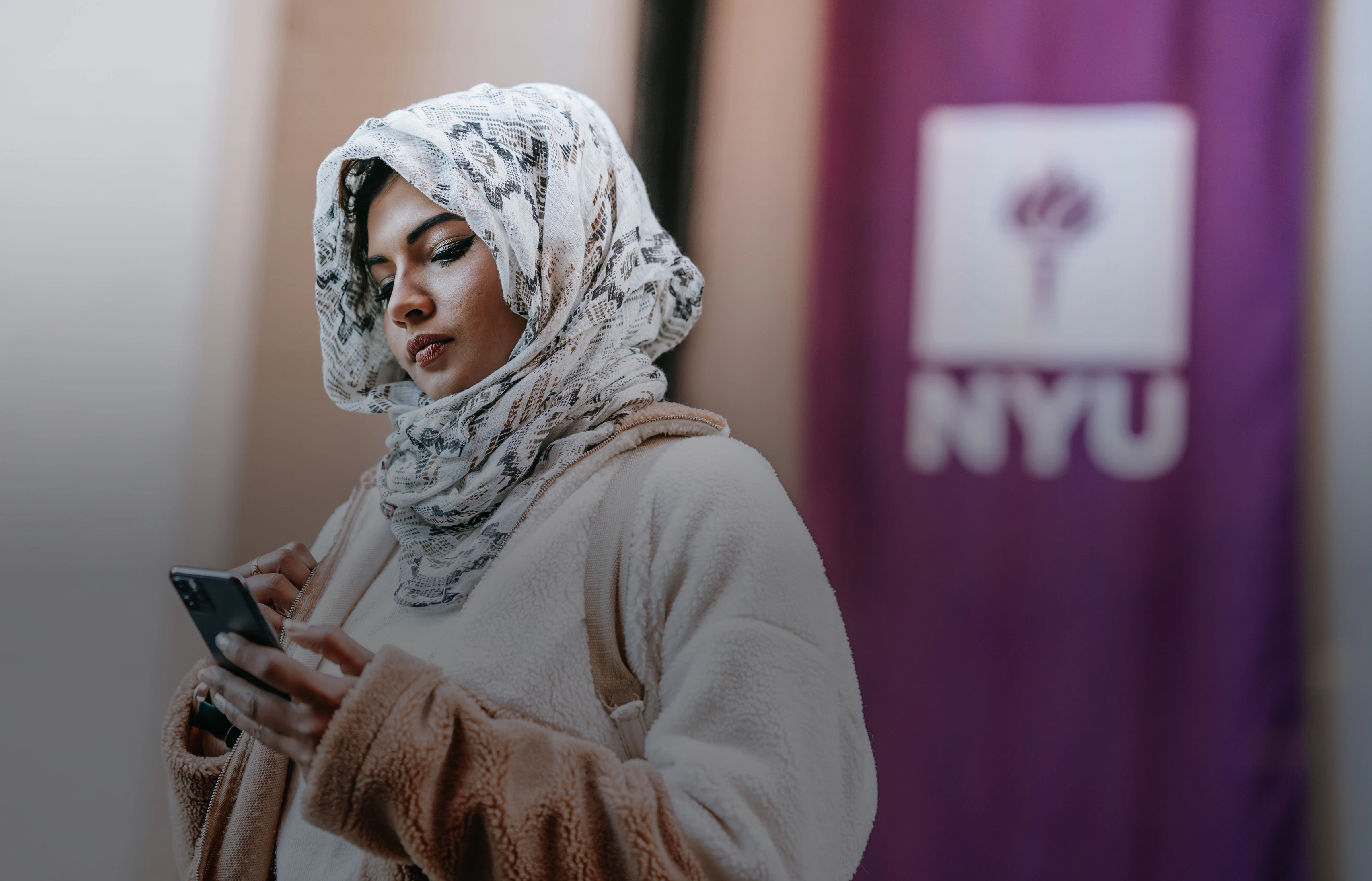 a woman in a hijab standing in front of a purple nyu banner