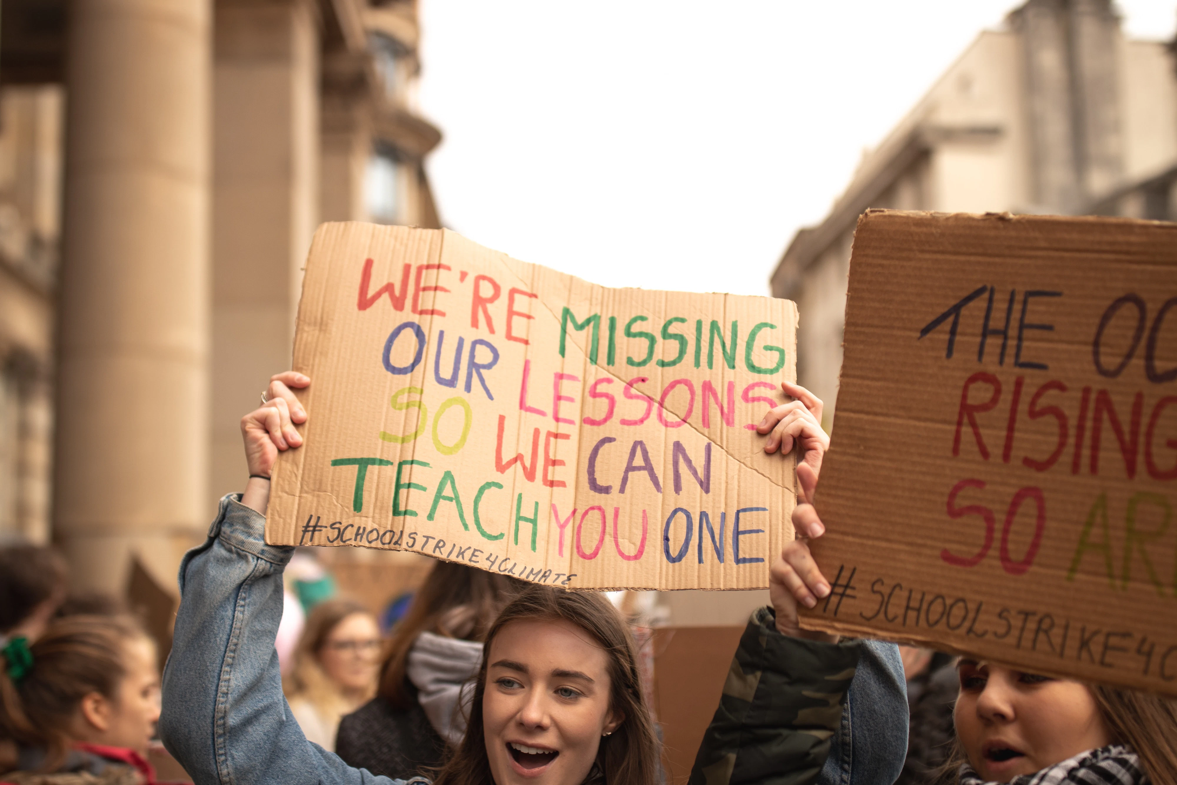 A protester holding a colorful sign that reads: "We're missing our lessons so we can teach you one"