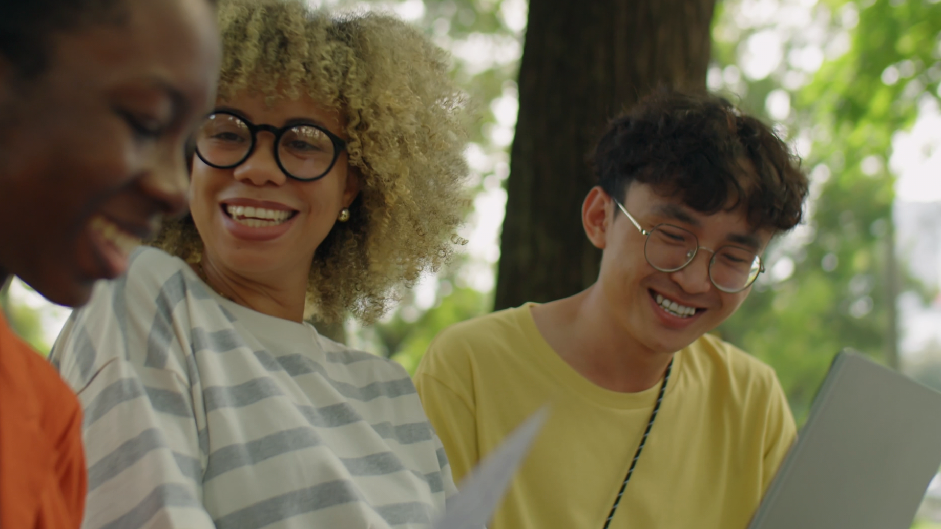 three students smiling, looking at a laptop 