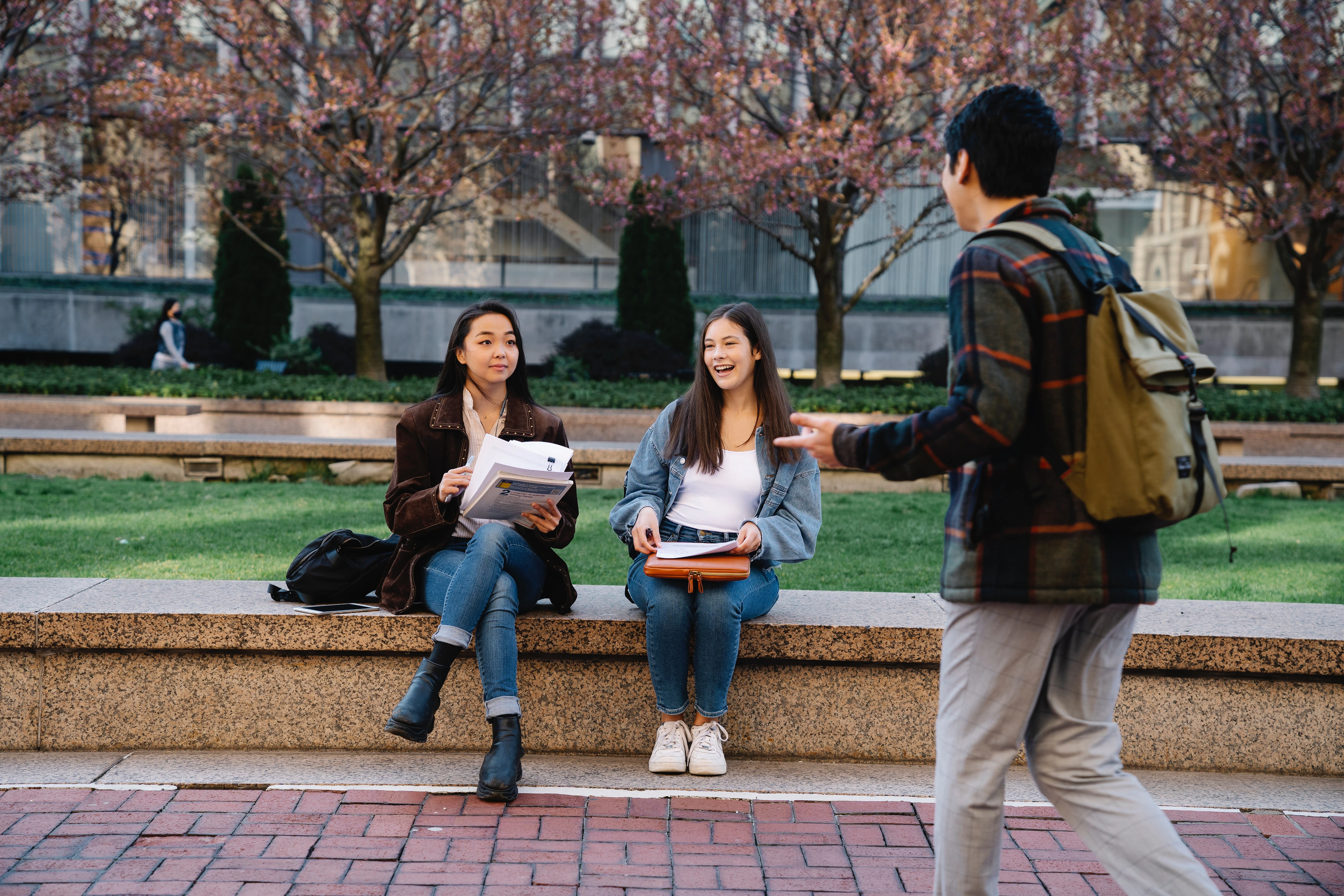 image of two students sitting on a bench as one passes by