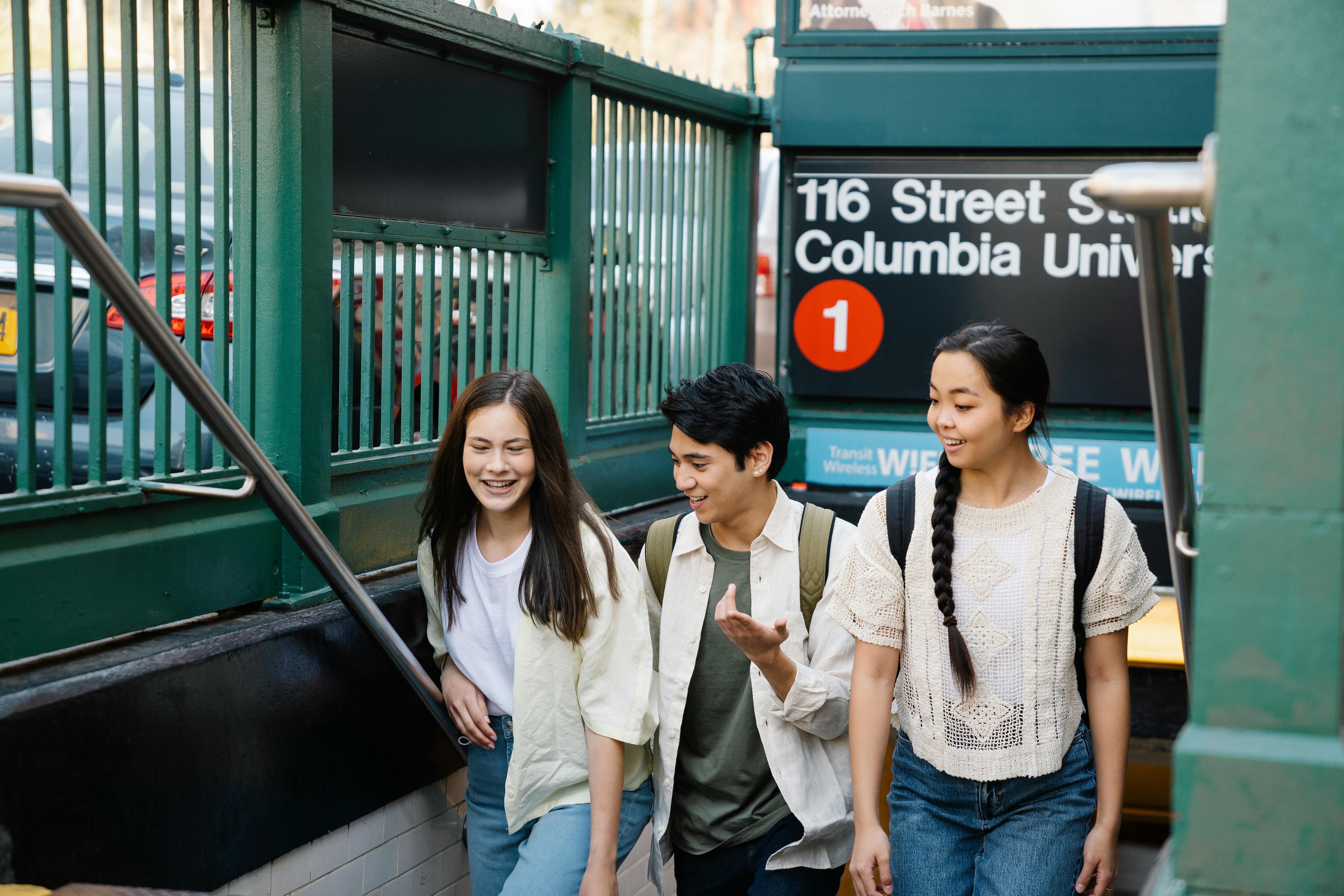 Three students walking out of subway with a sign that reads Columbia University 