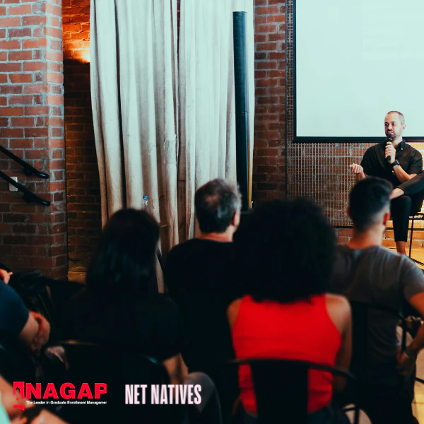 Man sitting on a stage, speaking into a microphone in front of an audience. Nagap and Net Natives logo in the corner.