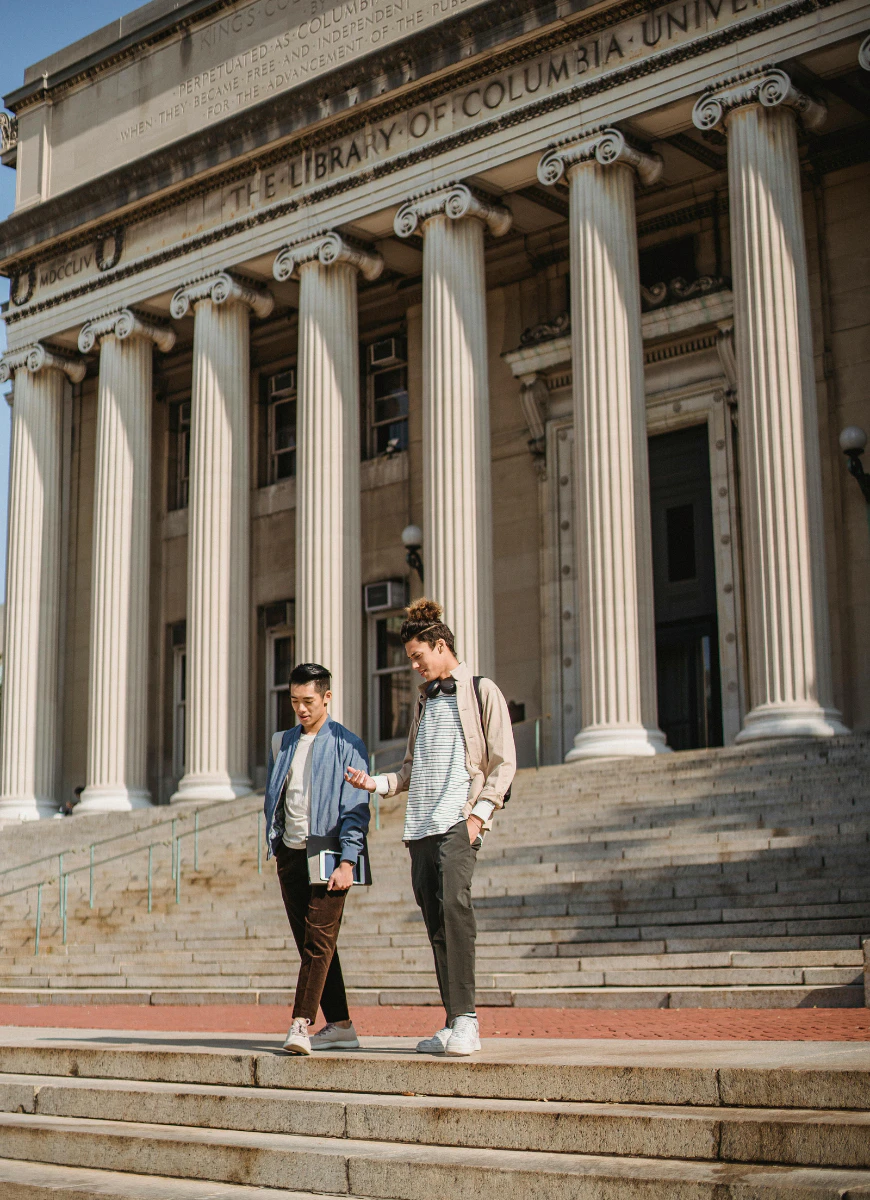 two students walking standing in front of a college building  