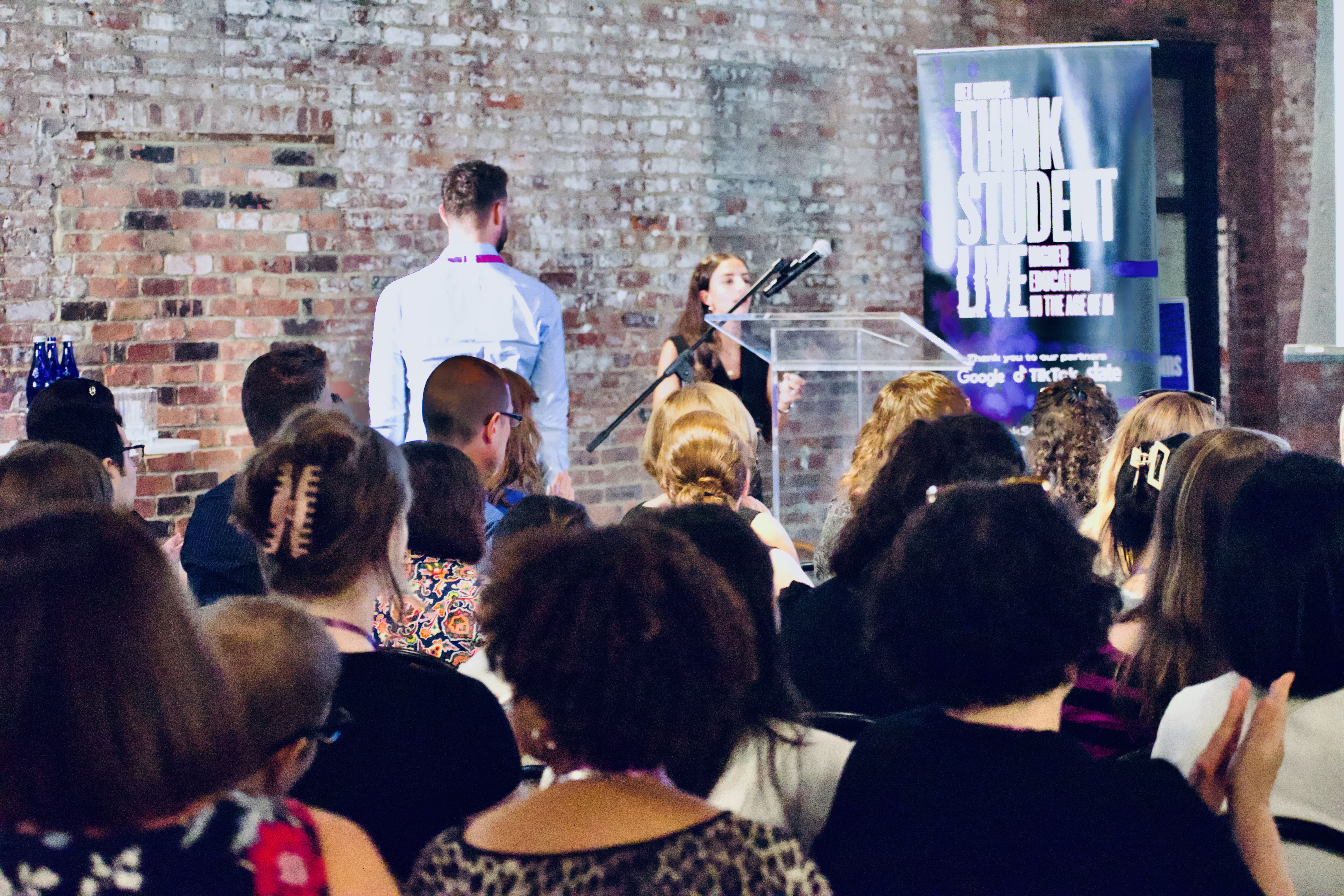 A crowd waits patiently for the event to start. In the background, Murray Simpson is walking towards the podium to give opening remarks.