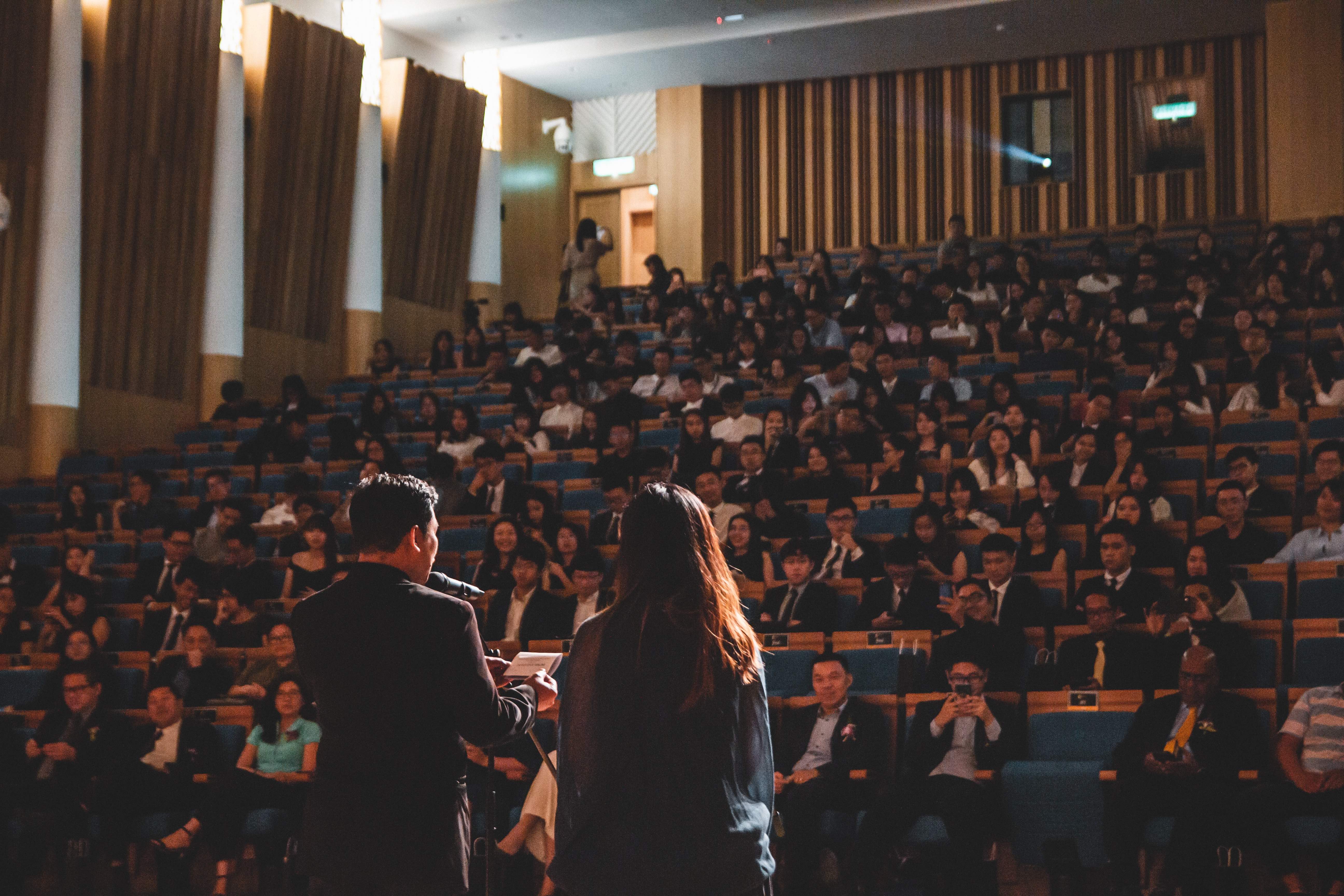Two speakers presenting in front of a crowded conference hall.