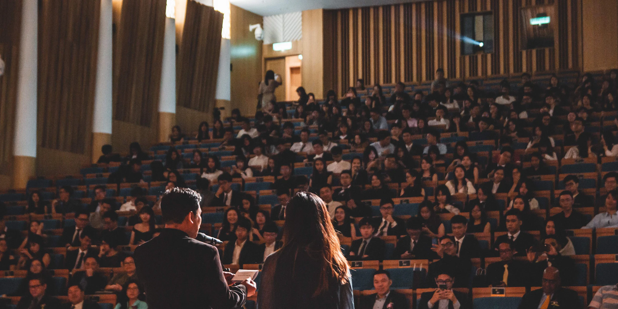 Two speakers presenting in front of a crowded conference hall.