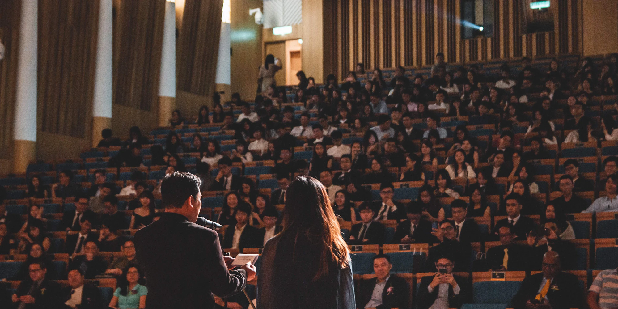 Two speakers presenting in front of a crowded conference hall.