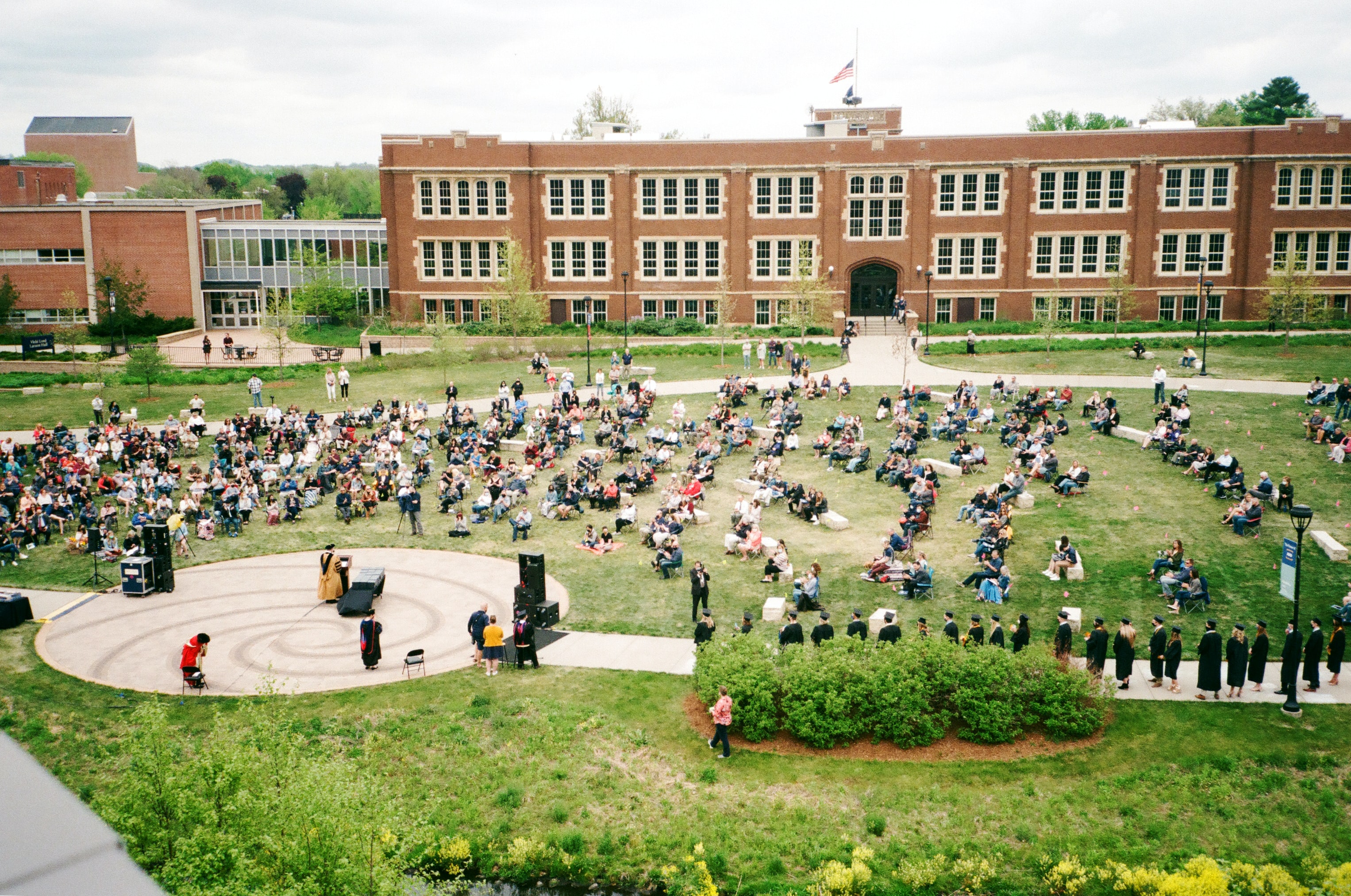 Students assembled outdoors on a college campus, listening to a speaker.