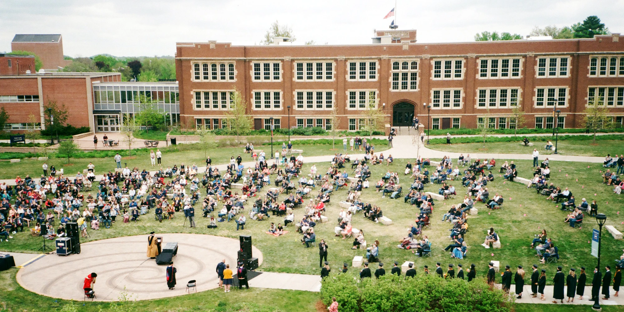 Students assembled outdoors on a college campus, listening to a speaker.